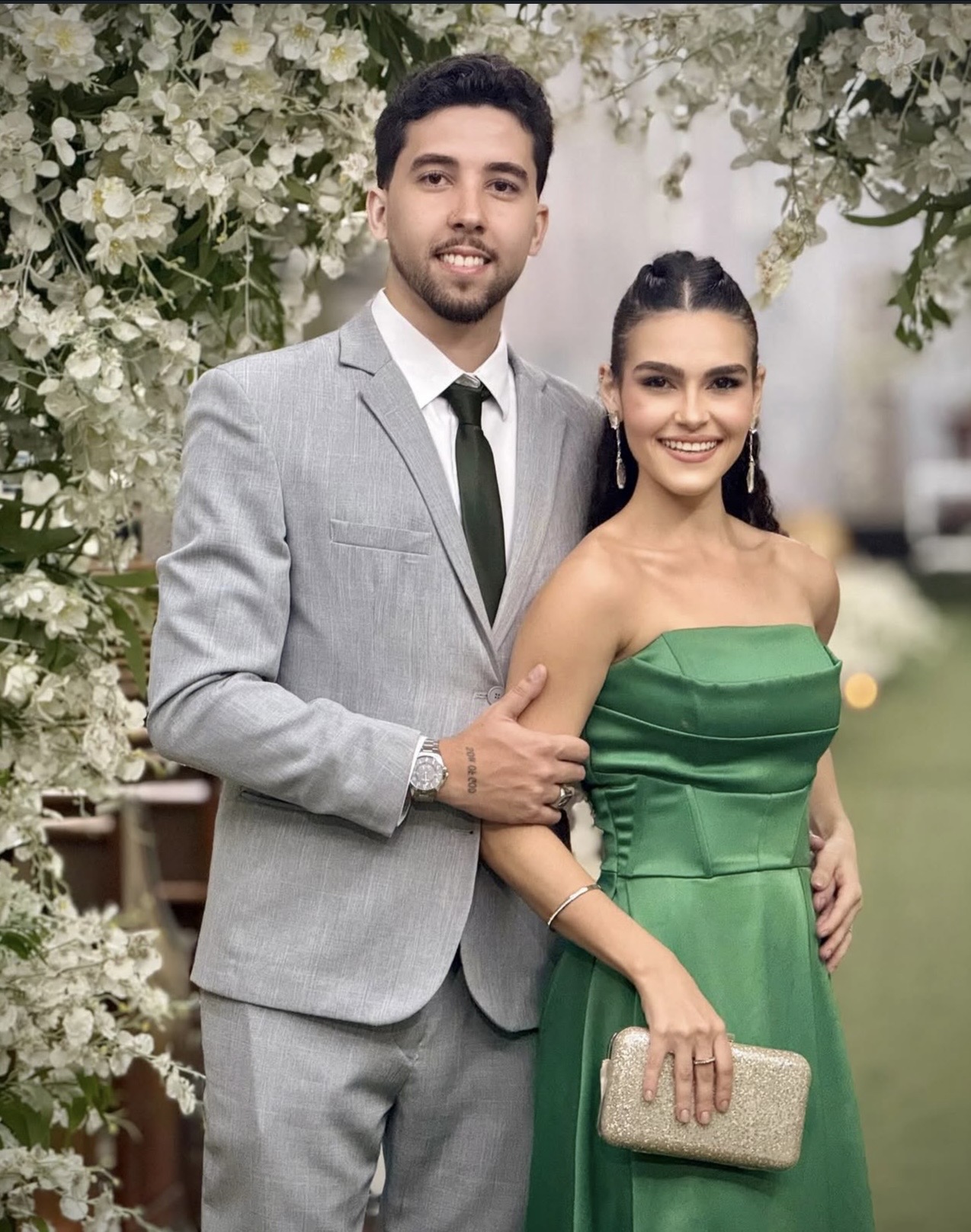 Rafael e Thaina juntos diante de um arranjo de flores brancas